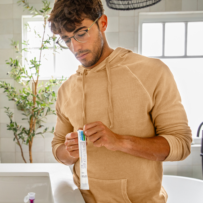An image of a man in his bathroom, opening the packaging for the nasal swab.