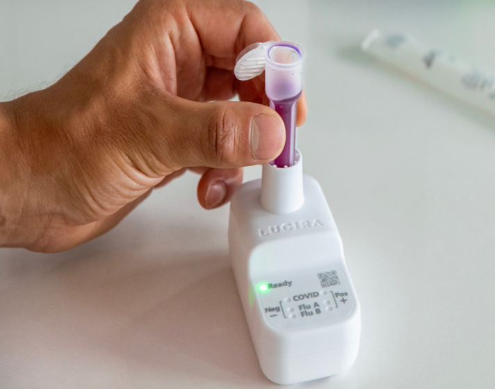 A hand is placing a vial with purple liquid into the white testing device.