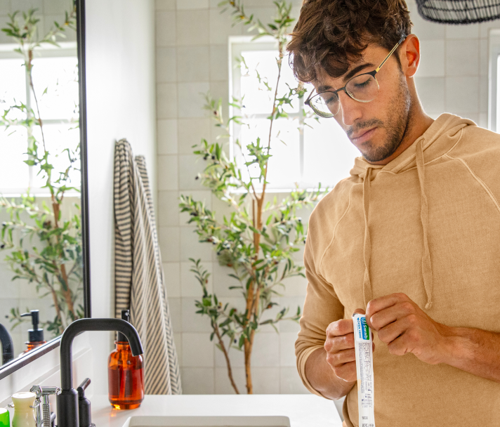 An image of a man in his bathroom, opening the packaging for the nasal swab.