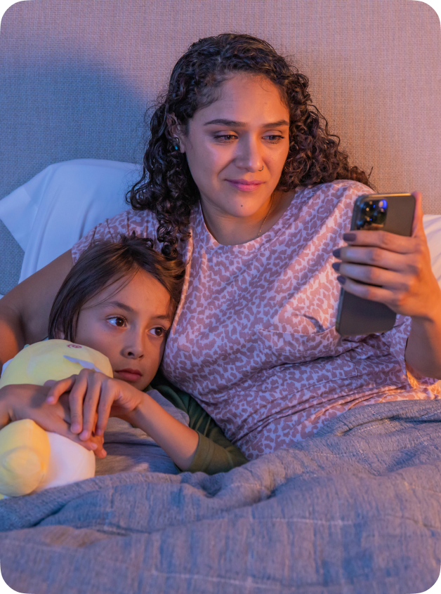 An image a happy mom lying in bed with her child, as she looks at her cell phone.
