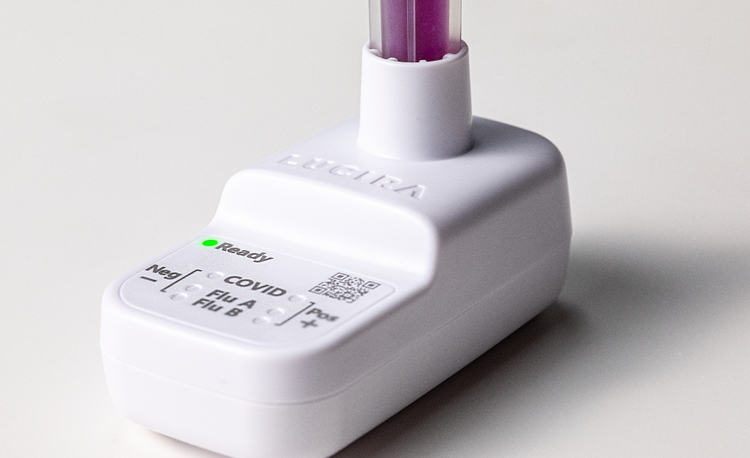A close-up shot of the white LUCIRA® by Pfizer device with the green ready light on and the vial with purple liquid sitting in the device.
