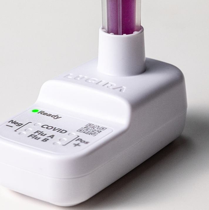 A close-up shot of the white LUCIRA® by Pfizer device with the green ready light on and the vial with purple liquid sitting in the device.