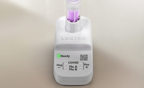 A close-up shot of the white LUCIRA® by Pfizer device with the green ready light on and the vial with purple liquid sitting in the device.