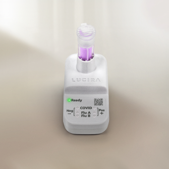 A close-up shot of the white LUCIRA® by Pfizer device with the green ready light on and the vial with purple liquid sitting in the device.
